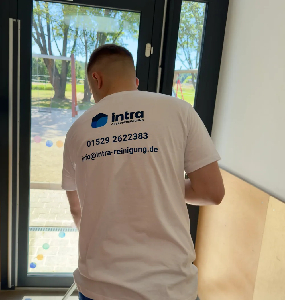 Mitarbeiter von intra reinigt eine Glastür, auf dem Shirt stehen Telefonnummer und Mailadresse