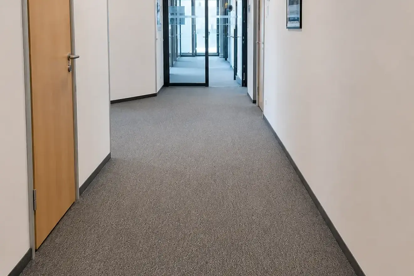 Gesaugter Büroflur mit Teppichboden und Blick zur Glastür am Ende