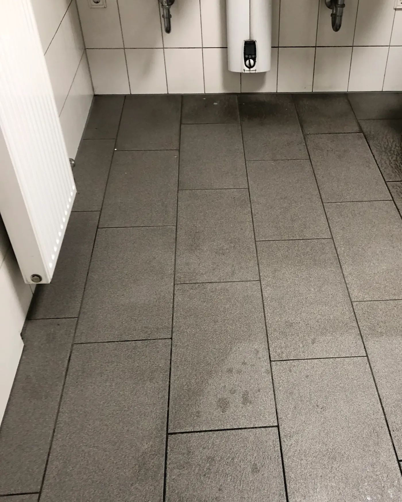 Derselbe Sanitärboden nach der Grundreinigung, die Fliesen sind wieder hell und gleichmäßig