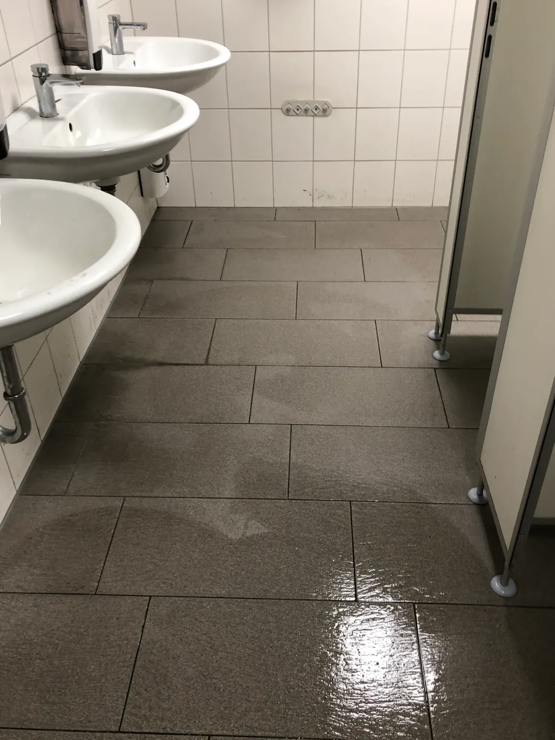 Sanitärraum mit drei Waschbecken und frisch gereinigtem Fliesenboden am Tag der Grundreinigung