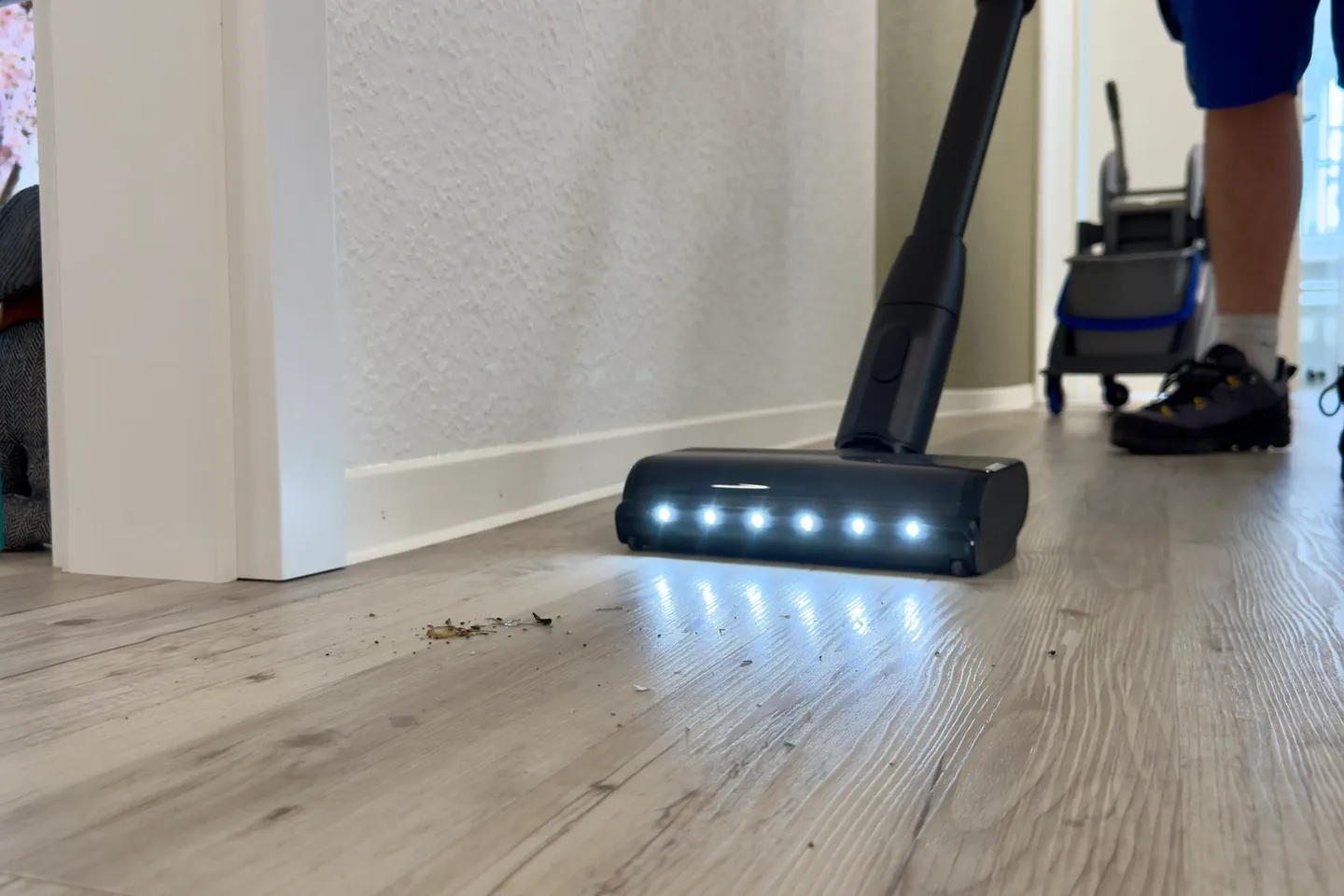 Akkusauger mit Bodenlicht auf hellem Holzboden, dahinter steht der Reinigungswagen von intra