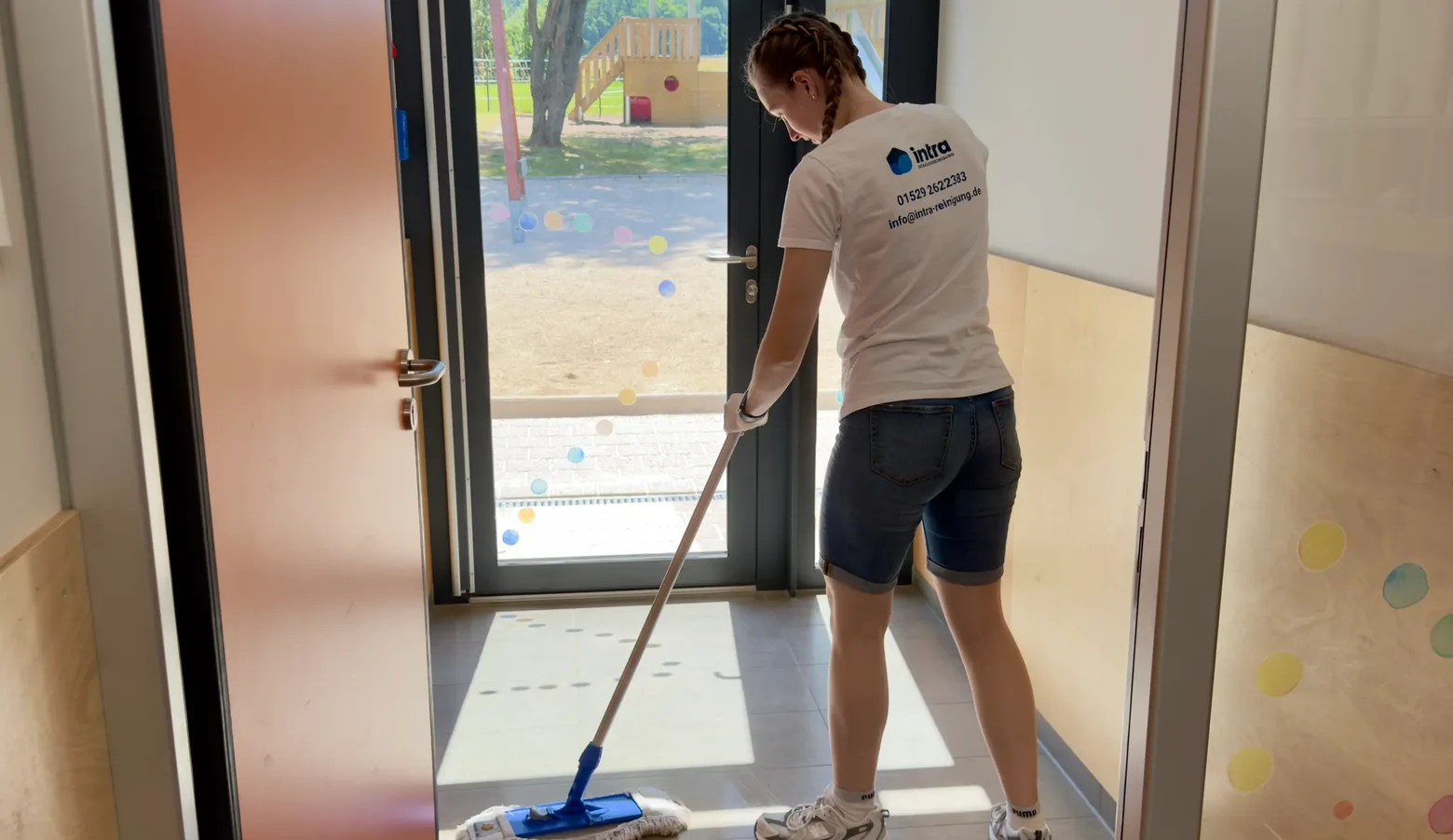 Eingangsbereich wird gewischt, Glastür und Boden im Vordergrund