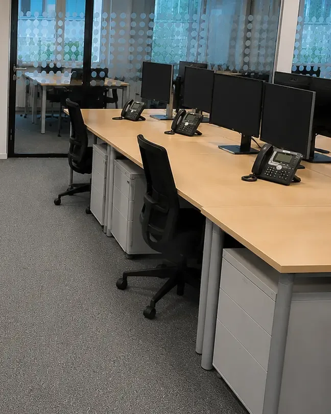 Zwei schwarze Bürodrehstühle mit Stoffpolster an einer Schreibtischreihe über grauem Teppichboden