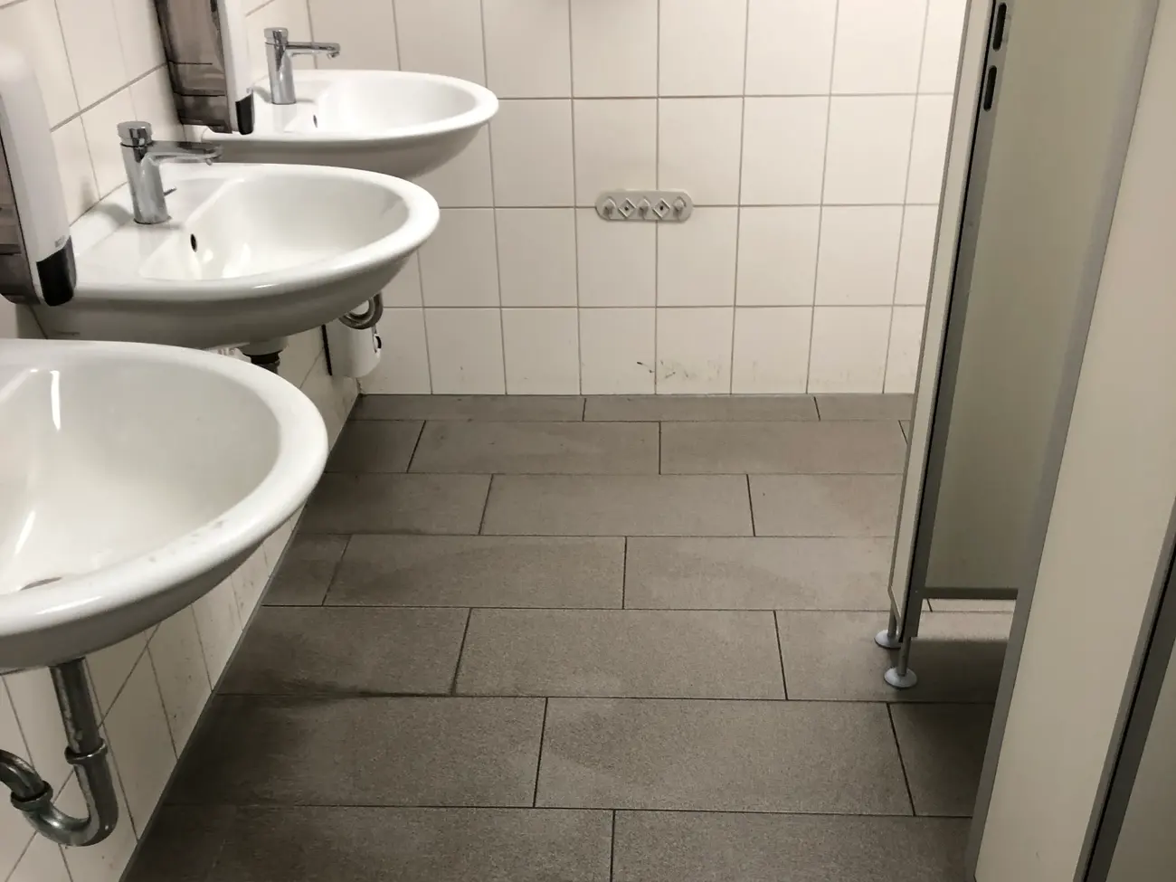 Frisch gewischter Sanitärbereich mit einer Reihe von Waschbecken und feuchtem Fliesenboden